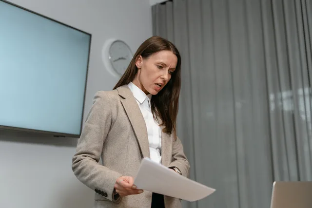 Professional woman in business attire reviewing documents indoors during a daytime meeting. PR response and issue handling